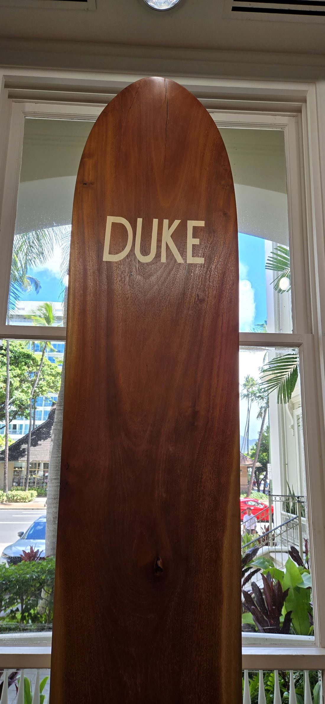 The nose of a koa board marked DUKE against the window glass.