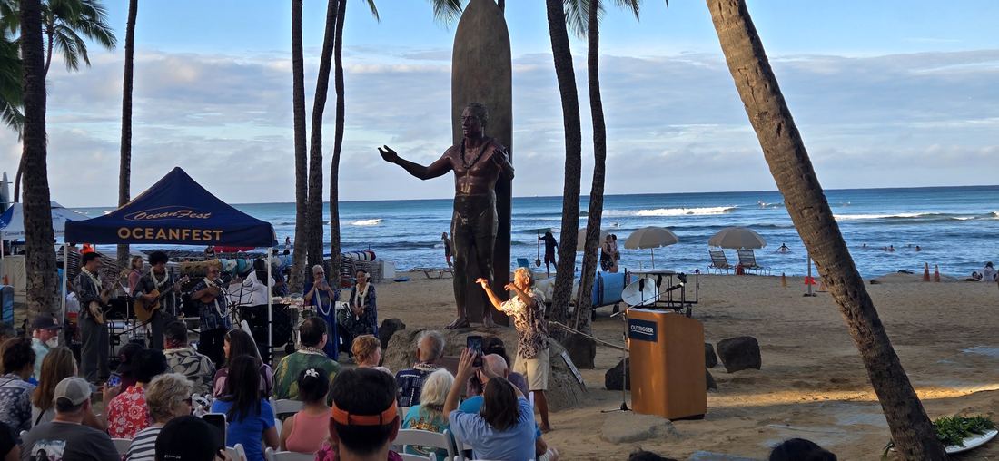 The bronze of Duke on Kūhiō Beach on his birthday, hung with lei, a crowd gathered at sunrise.