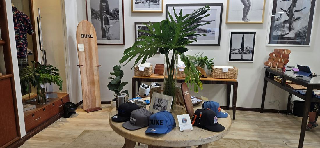 A round wooden table set with caps under a monstera, framed photographs on the wall behind.